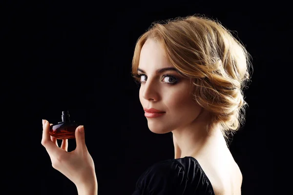Hermosa joven con botella de perfume sobre fondo negro — Foto de Stock