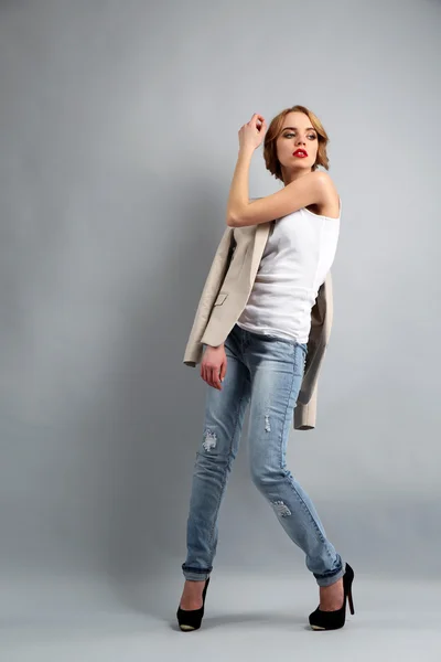 Bella giovane donna in giacca e jeans in posa su sfondo chiaro — Foto Stock