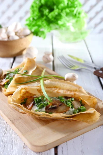 Pancakes with creamy mushrooms on cutting board on wooden table, closeup — Stock Photo, Image