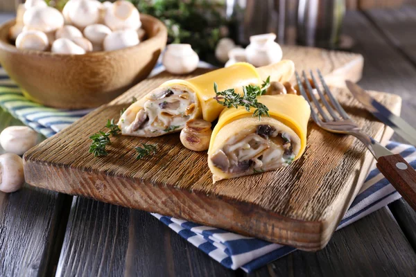 Pancakes with creamy mushrooms on cutting board on wooden table, closeup — Stock Photo, Image