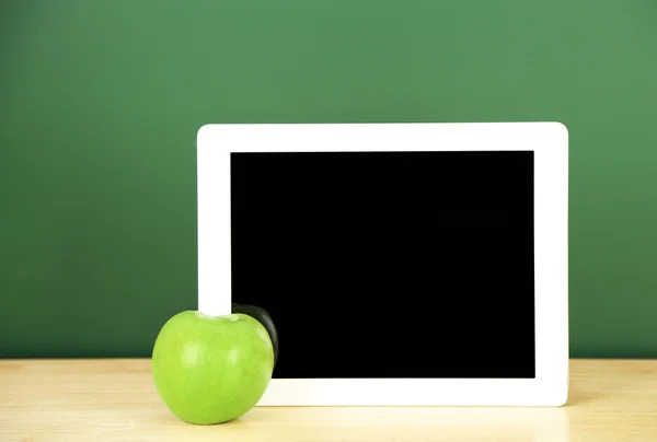 Tablet op tafel, op groene krijtbord achtergrond — Stockfoto