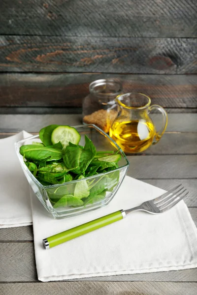 Glass bowl of green salad with cucumber and spinach on wooden background — Stock Photo, Image