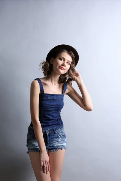 Retrato de modelo hermoso en ropa vaquera y sombrero sobre fondo gris —  Fotos de Stock