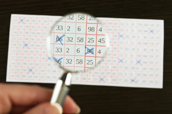 Vrouwelijke hand met Vergrootglas analyseren loterij ticket, close-up — Stockfoto
