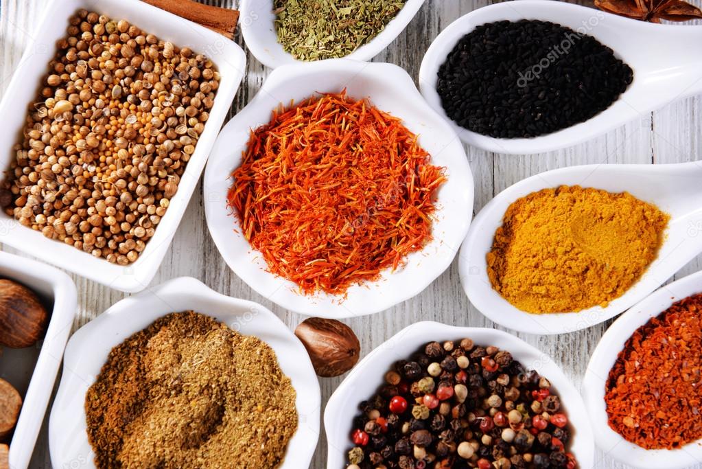 Different kinds of spices in ceramics spoons, close-up, on wooden background