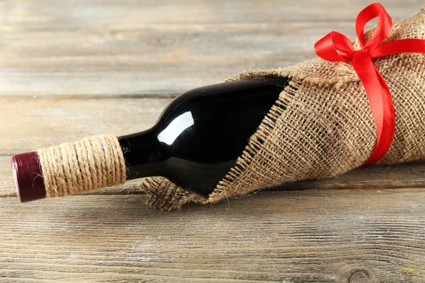 Red wine bottle wrapped in burlap cloth on wooden planks background — Stock Photo, Image