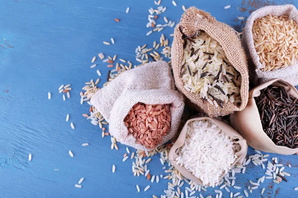 Diferentes tipos de arroz em sacos no fundo de madeira — Fotografia de Stock
