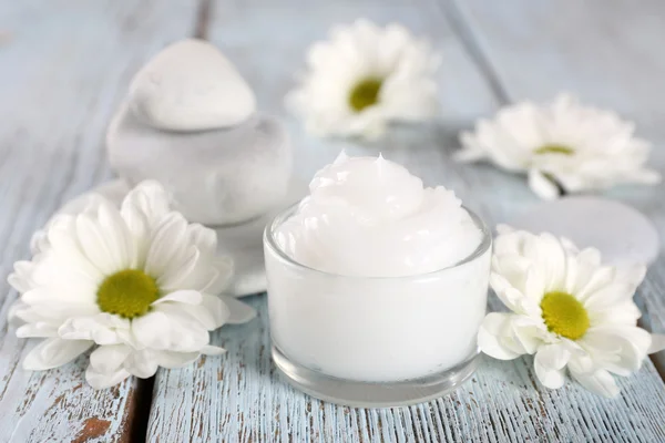 Creme cosmético com flores e pedras de spa em fundo de madeira — Fotografia de Stock