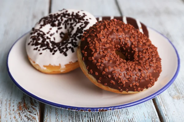 Delicious donuts with icing on plate on wooden background — Stock Photo, Image