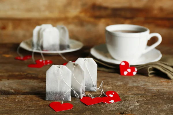 Serce torebkę Tagi i filiżankę herbaty z na drewniane tła — Zdjęcie stockowe