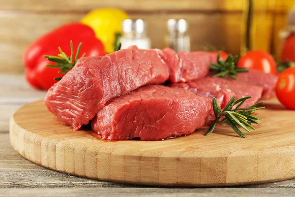 Steak daging sapi mentah pada potongan papan dengan sayuran dan rempah-rempah pada latar belakang kayu — Stok Foto