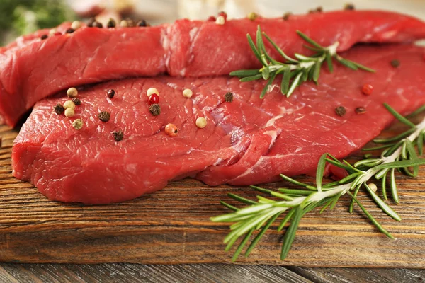 Raw beef steak with rosemary and spices on cutting board on wooden background — Stock Photo, Image