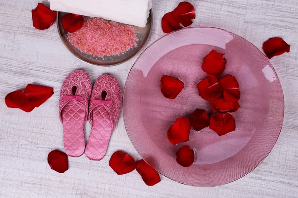 Spa bowl with water, rose petals, towel and slippers on light background. Concept of pedicure or natural spa treatment — Stock Photo, Image