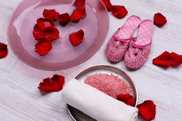 Spa bowl with water, rose petals, towel and slippers on light background. Concept of pedicure or natural spa treatment — Stock Photo, Image