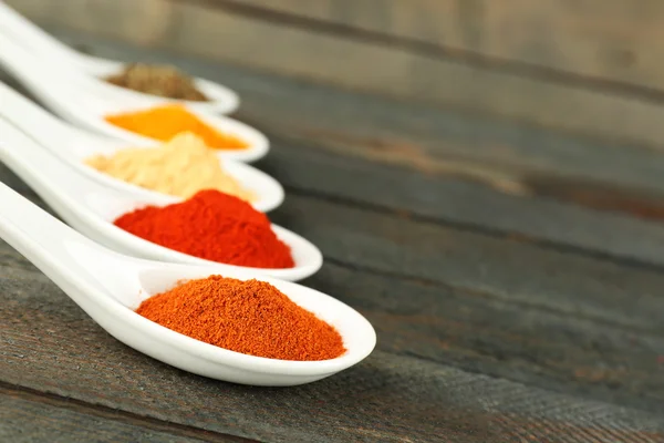 Different kinds of spices in spoons on wooden background — Stock Photo, Image