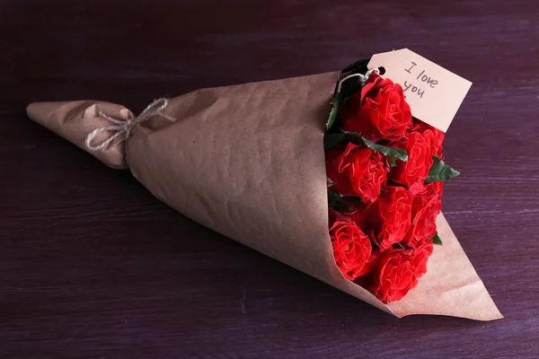 Boeket van rode rozen met tag gewikkeld in papier op houten achtergrond — Stockfoto