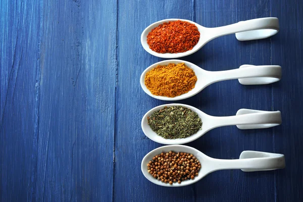 Different kinds of spices in ceramics spoons, close-up, on color wooden background — Stock Photo, Image