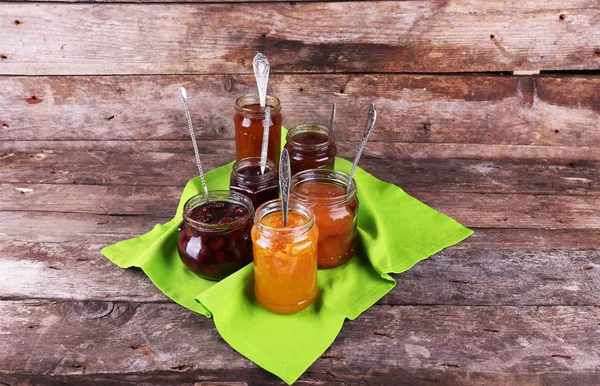 Jars of tasty jam with napkin on wooden background — Stock Photo, Image