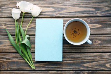 Çay ve beyaz laleler bardak ile ahşap arka plan üzerinde kitap