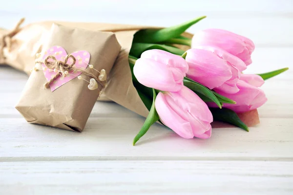 Beautiful pink tulips in paper with present box on wooden background — Stock Photo, Image