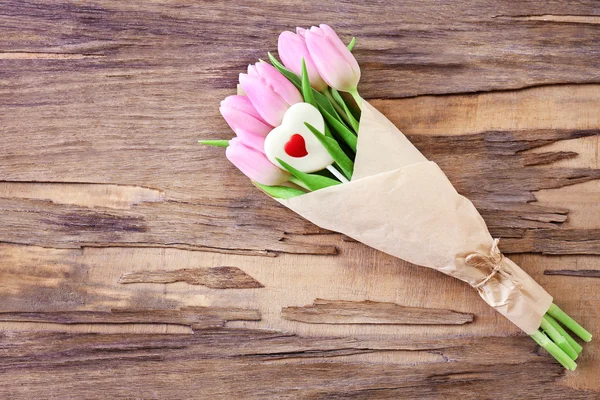 Piękne różowe tulipany w papier z słodkie serca na tle drewniane — Zdjęcie stockowe