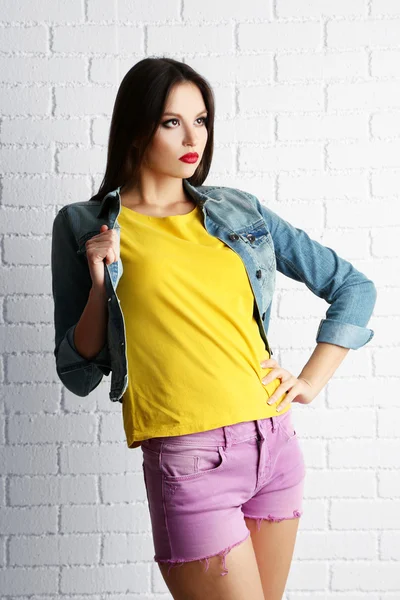 Chica bonita vestida en estilo casual posando sobre fondo de pared de ladrillo blanco —  Fotos de Stock