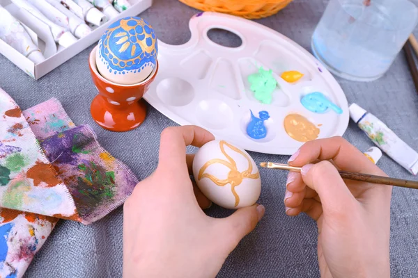 Живопись пасхальных яиц женскими руками на цветном фоне скатерти — стоковое фото