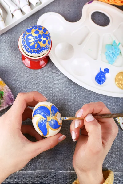 Painting Easter eggs by female hands on colorful tablecloth background — Stock Photo, Image