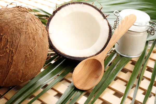 Kokos met bladeren en kokosolie in pot op houten achtergrond — Stockfoto