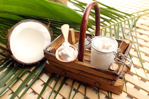 Coconut with leaves and coconut oil in jar on wooden background — Stock Photo, Image