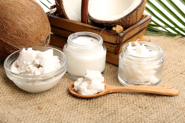 Coconut with jars of coconut oil and  cosmetic cream on sackcloth on natural background