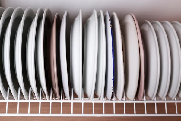 Clean plates drying on metal dish rack on shelf — Stock Photo, Image