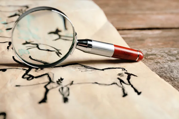 Rock paintings with magnifier on paper on wooden table close up — Stock Photo, Image