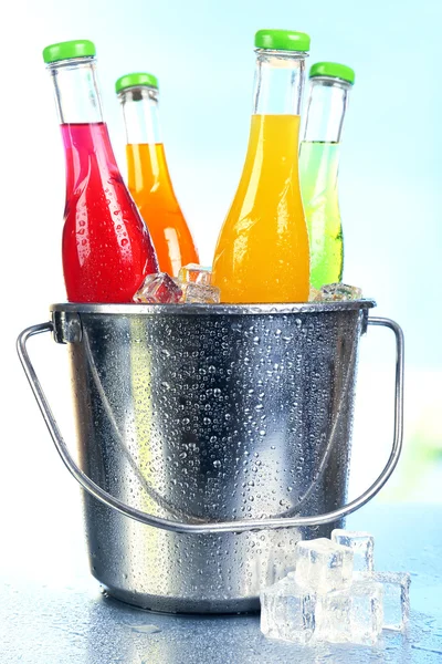 Botellas de bebida sabrosa en cubo de metal con hielo sobre fondo brillante —  Fotos de Stock