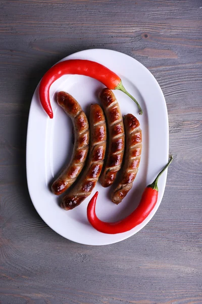 Grilled sausages on plate with chili pepper on table close up — Stock Photo, Image