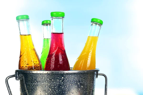Bottles of tasty drink in metal bucket with ice on bright background — Stock Photo, Image