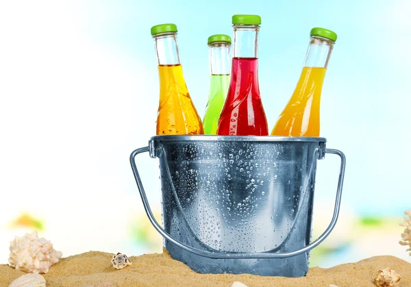 Flaschen leckeres Getränk in Metalleimer mit Eis auf Sand auf hellem Hintergrund — Stockfoto