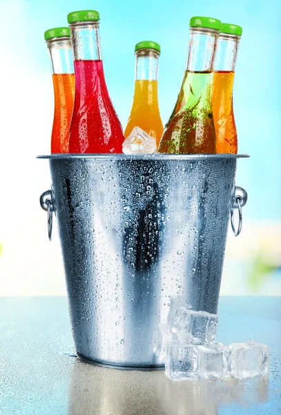 Bottles of tasty drink in metal bucket with ice on bright background — Stock Photo, Image