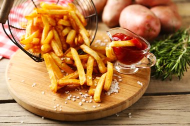 Ahşap masa arkasında metal sepetin içinde patates kızartması.