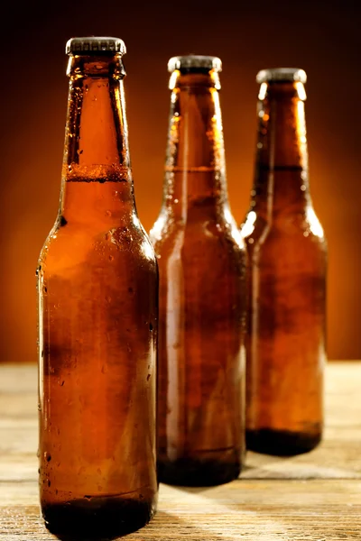 Glazen flessen bier op houten tafel op donkere achtergrond — Stockfoto