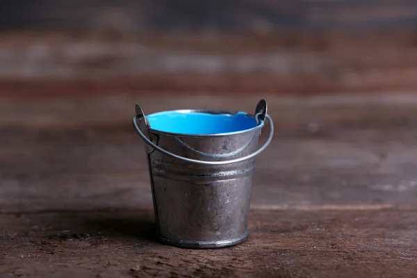 Metal bucket with colorful paint on wooden background