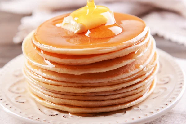 Deliciosos panqueques con miel en el plato en primer plano de la mesa — Foto de Stock