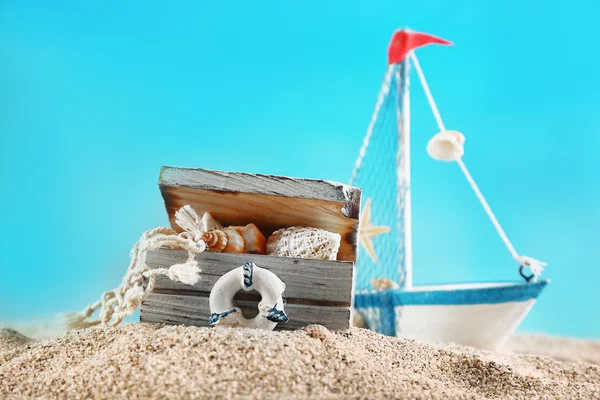 Морской натюрморт с игрушечной моделью корабля на песке на синем фоне — стоковое фото