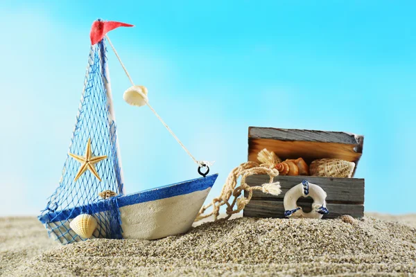 Marine still life with toy model of ship on sand on blue background — Stock Photo, Image