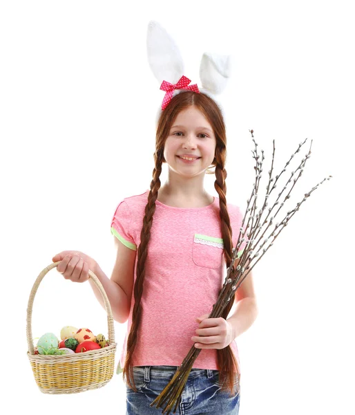 Beautiful little girl holding wicker basket with Easter eggs and pussy-willow branches, isolated on white — Stock Photo, Image