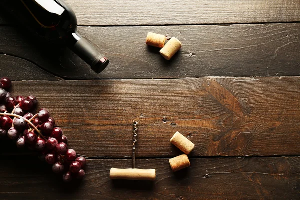 Glazen fles wijn met kurken en druiven op houten tafel achtergrond — Stockfoto