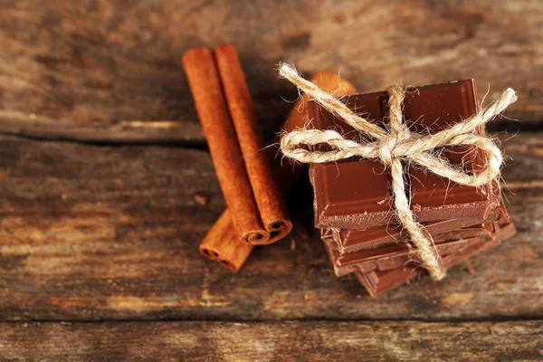 Stukken van chocolade met kaneelstokjes op houten achtergrond — Stockfoto