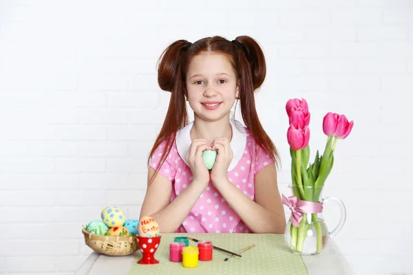 Cute girl decorates Easter eggs, on light background — Stock Photo, Image