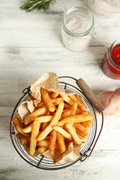 Frites savoureuses dans un panier en métal sur fond de bois de couleur — Photo