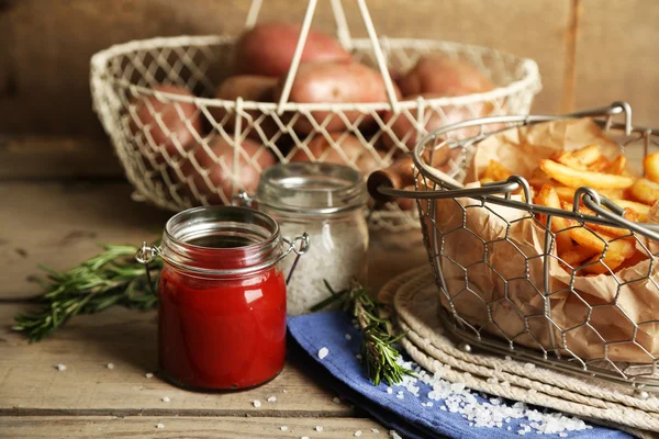 Tasty french fries and fresh potatoes in metal baskets on wooden table background — Stock Photo, Image